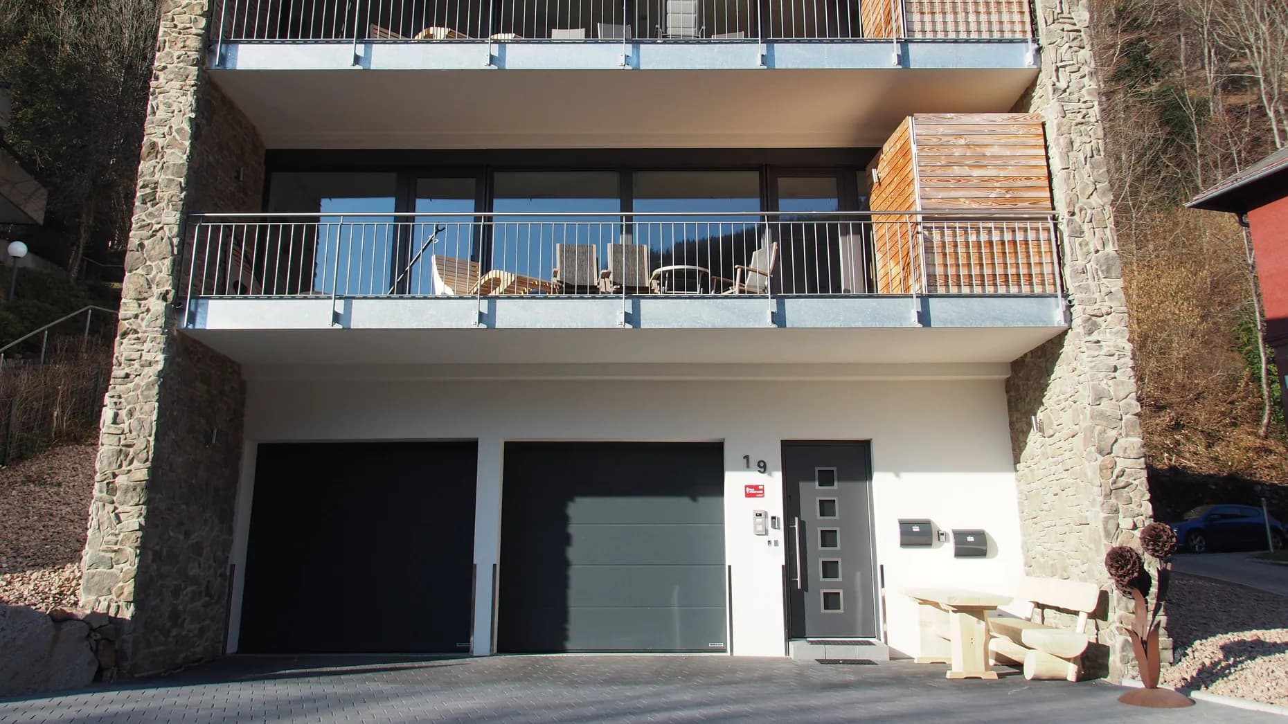 Eingangsbereich von Haus LuFeTo mit Haustür, zwei Garagen und Sitzbank aus Holz